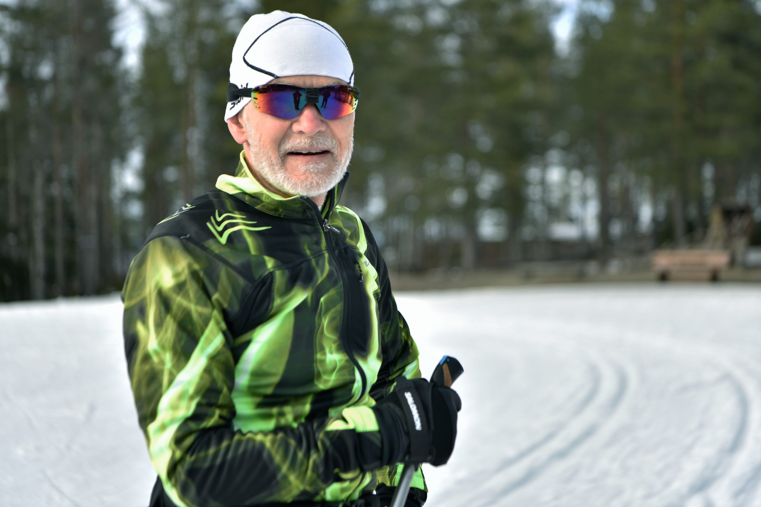Man I färglada glasögon och skidutrustning i ett skidspår ler mot kameran.