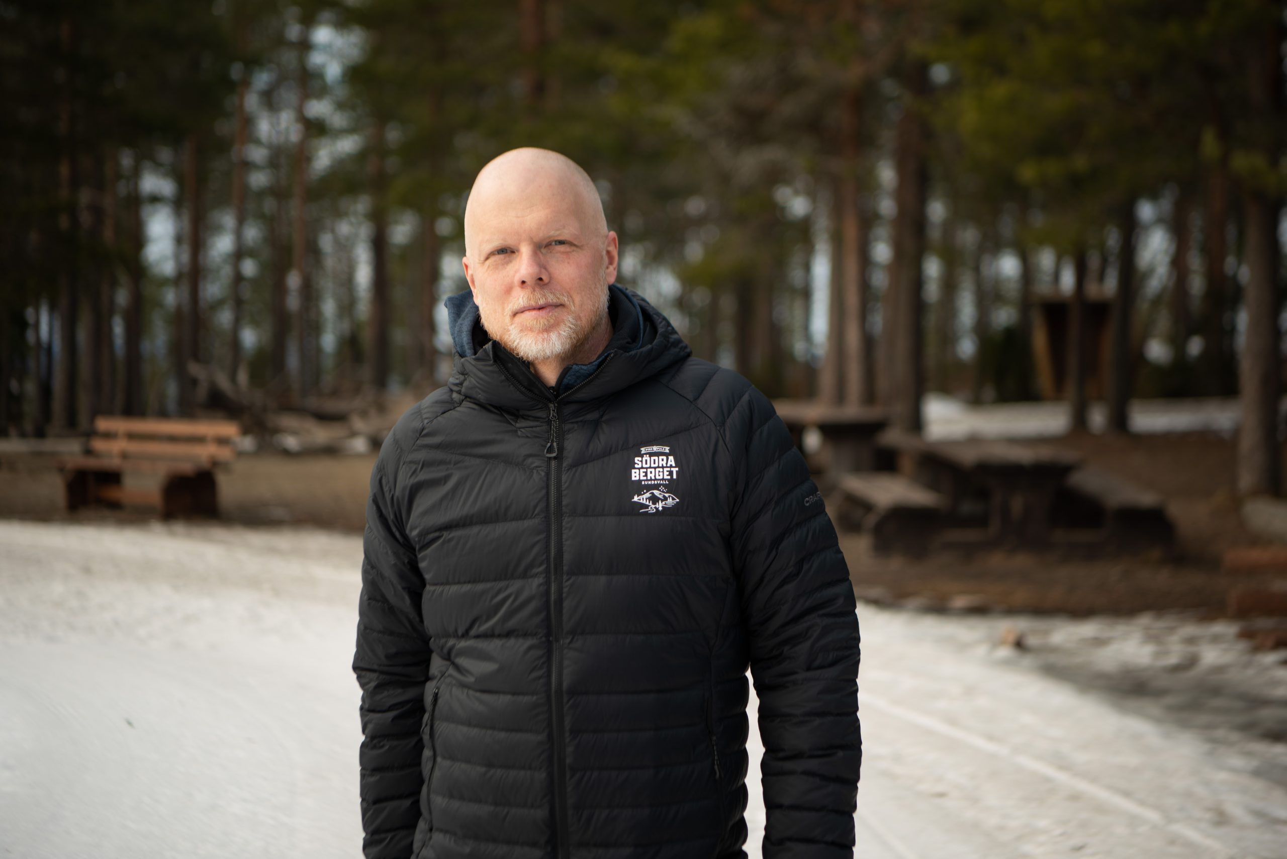 Man I svart jacka står framför snö och skog.